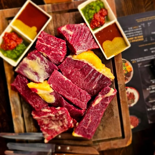 Raw beef cuts with yellow and white fat, served with colorful sauces on a wooden board.