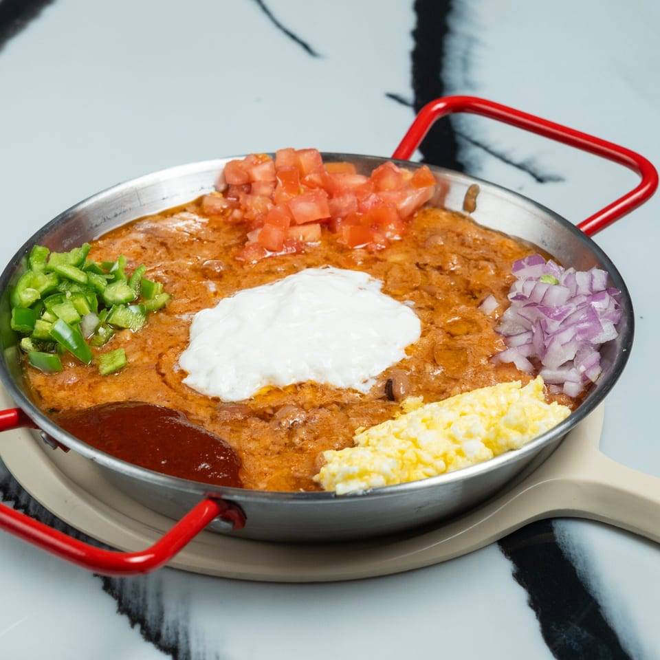 Ethiopian ful medames in a pan with diced tomatoes, green peppers, onions, scrambled eggs, and sour cream.