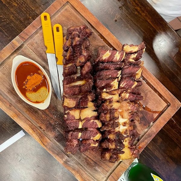 Ethiopian Gored Gored, raw beef cubes, with two yellow-handled knives and a dipping sauce.