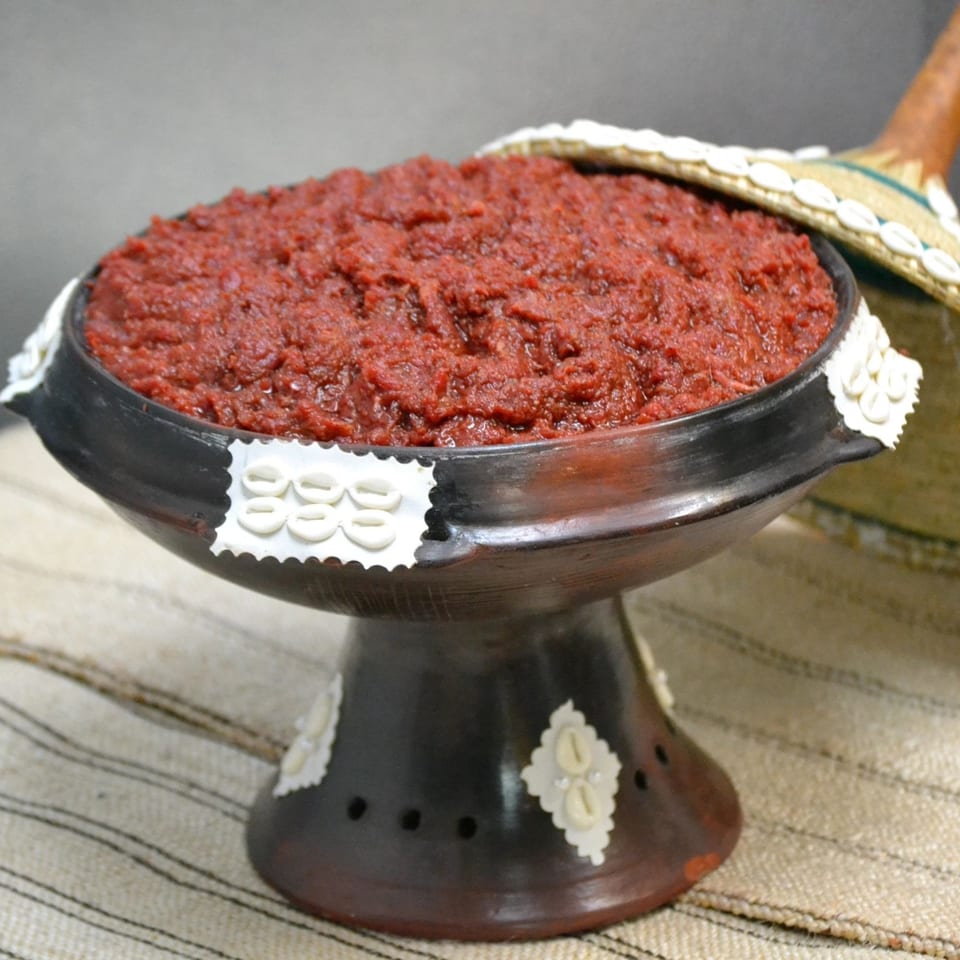 A dark, ornate Ethiopian serving bowl filled with a rich, red berbere spice paste.