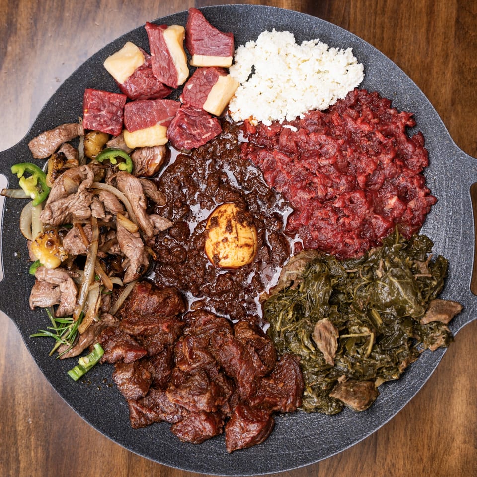 An Ethiopian platter with various meat dishes, collard greens, cottage cheese, and a hard-boiled egg.