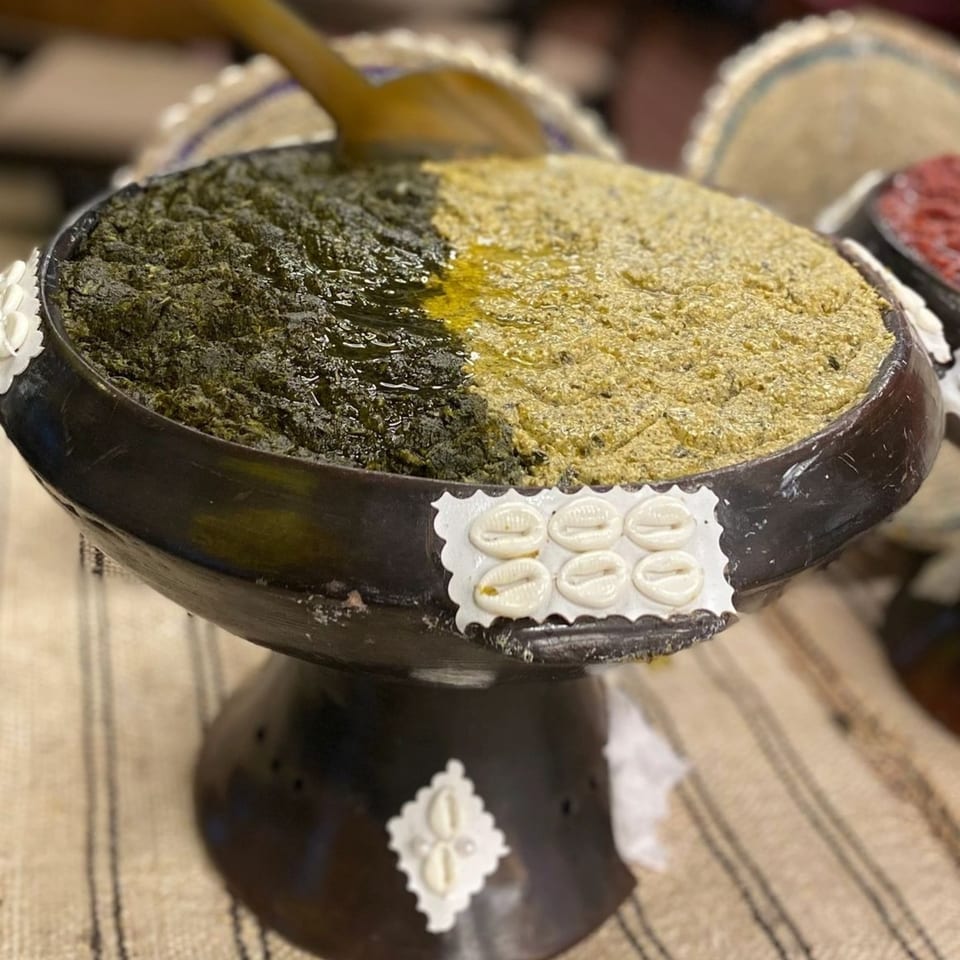 A black bowl filled with two types of Ethiopian food, one green and one yellow, with a wooden spoon.