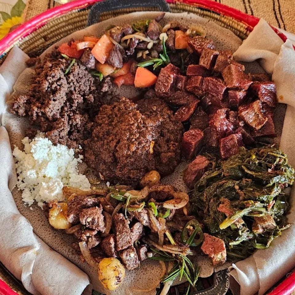 A large platter of Ethiopian injera bread topped with various meat and vegetable dishes.